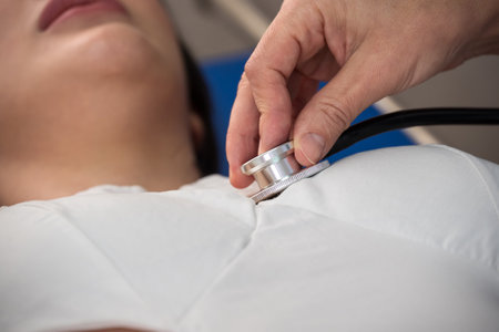 Cropped image of female doctor hand using medical stethoscope for checking heartbeat rate of woman patient on bed in hospital . Healthcare and insurance conceptの写真素材