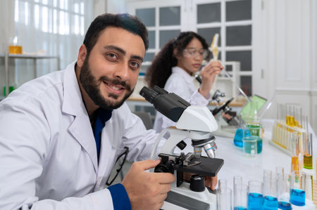 Smiling scientist with beard in white laboratory coat working with microscope for research in scientific research laboratoryの写真素材