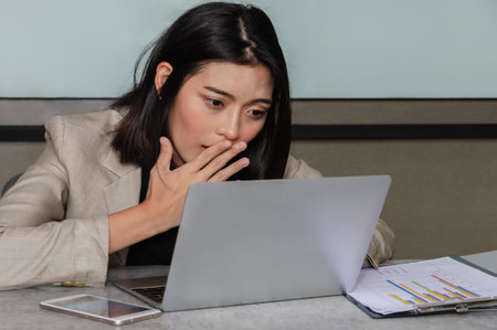 Surprised Asian businesswoman using her laptop at meeting room, covering her mouth out of courtesy. Business and office concept.の写真素材