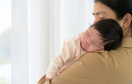 Adorable newborn baby girl sleeping on mom shoulder next to white curtain window. Young Asian mother hold infant 1 month with love, gently and happy. Safe with mom hug and healthy newborn baby conceptの写真素材