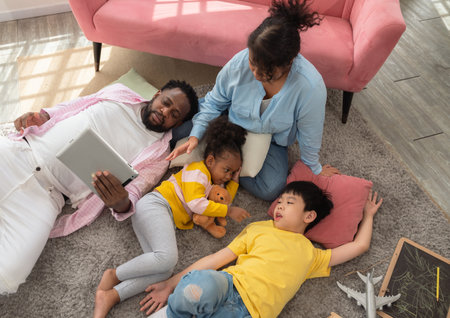 Happy family spending leisure time at home. African father and  children lying on floor rug while...
