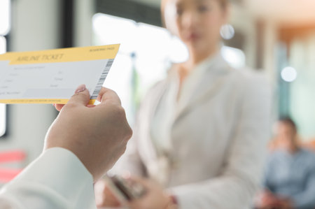 Ground attendant woman hand holding airline boarding ticket in front of businesswoman traveler at airport check in counterの写真素材