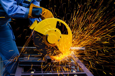 Worker cuts metal by electric circular saw. Fountain of grinding metal sparks. Industrial working...