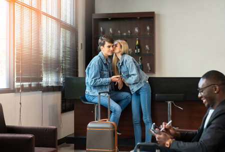Caucasin couple in denim outfits shares sweet moment in airport lounge area. Woman kisses  man on cheek while sitting at bar counter with luggageの写真素材