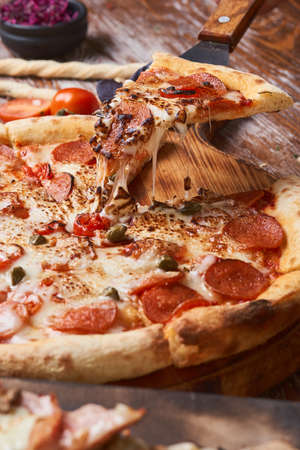 Italian pizza on a wooden table. A piece of hot pizza with cheese stretching.の写真素材
