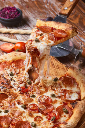 Italian pizza on a wooden table. A piece of hot pizza with cheese stretching.