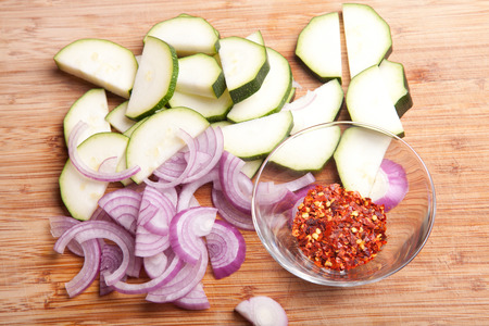 copped courgette, red onion and dried chili on wooden chopping boardの写真素材