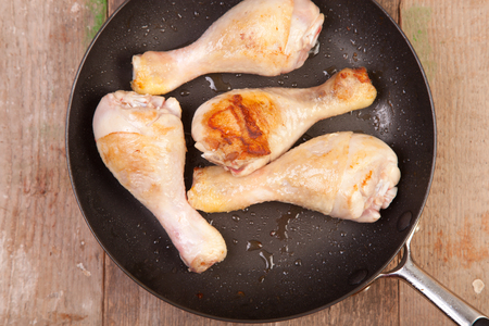 fryed chicken drumsticks in frying pan on wooden tableの写真素材