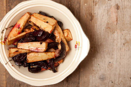 roast parsnips and beetroots in a bowl on wooden tableの写真素材