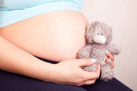 Pregnant women holding a teddy on her laps, horizontal picture