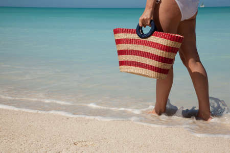 woman walking with bag at white sand beachの写真素材