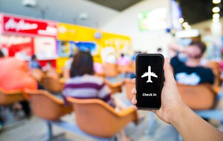 Cell phone in hand with airplane icon and blur airport background on travel concept 
