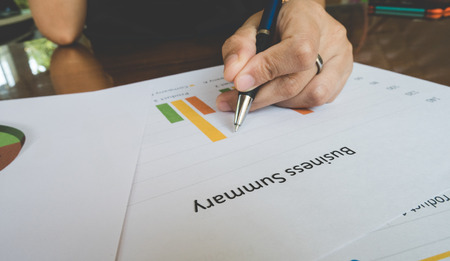 Working woman hand holding pen with Business summary or Business plan report with Charts and graphs in Business concept, vintage styleの写真素材