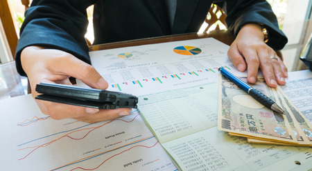 Business woman hand hold pen and use calculator on Statement or financial report in business concept.の写真素材