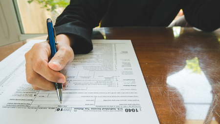Business woman hand hold pen fill in the details on the tax forms paper in business conceptの写真素材