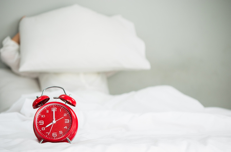 The red clock stand on the bed.の写真素材