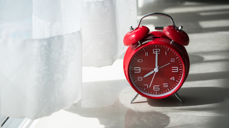 Red table clock in the weekend mornning at window with curtains and Vertical blindsの写真素材