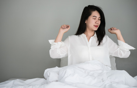 Asian women wake up from sleep. are  stretch herself  in the morning on the weekend sit on the bed at luxury room in Relax and weekend conceptの写真素材