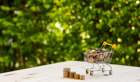 Coin in shopping cart on wood table with bokeh background in finacial or business conceptの写真素材