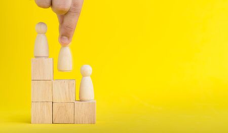 The hand is picking or select wood figure on the wooden Stacked in human resource management concepts Teamwork.Success Leadership,Business Progress and Competition on yellow backgrond and copy spaceの写真素材