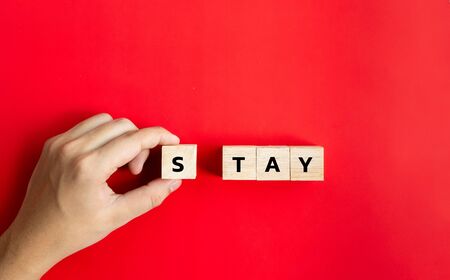 Hand hold on to the wood cube and text the word "Stay" In the concept, stay at home to stop the spread. During the corona virus outbreak or COVID-19 on red backgroundの写真素材