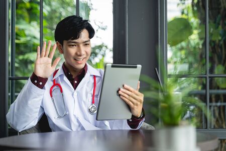 Asian Doctors are using tablets to greet patients via video call. A new normal of medical can treat, follow up illnesses and consult remote patients using the internet of things technologyの写真素材