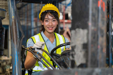 A female engineer is controlling a forklift in a spare parts factory. A smiling woman is deliberately practicing machine control in a factory in Industrial Engineering worker conceptの写真素材