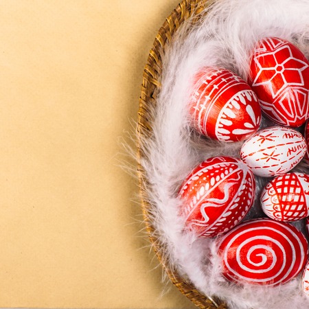Easter red eggs with folk white pattern lay on feather into basket in the right side of retro paper. Ukrainian traditional eggs pisanka and krashanka.の写真素材
