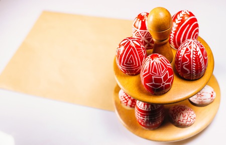 Closeup Easter red eggs with folk white pattern lay around on stand for eggs which stand on old of paper on white background.の写真素材