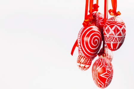 Bundle of Easter eggs with folk Ukrainian pattern hang on red ribbons from right side on white background.の写真素材