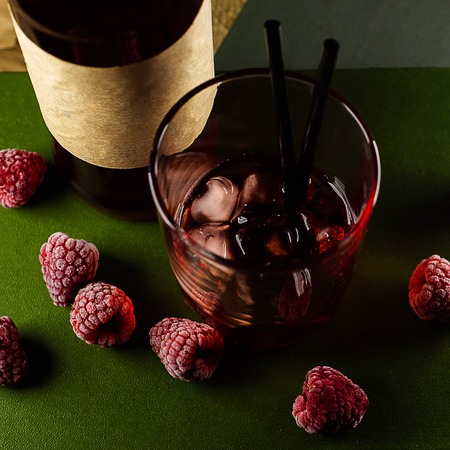 Part of bottle and glass with craft raspberries alchol drink with berries around on background. Top...