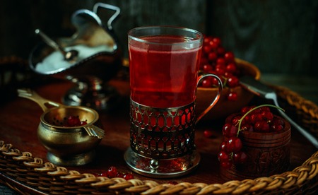 Still life in vintage style. Close up glass and decanter with red current tea or fruit-drink on wicker trayの写真素材