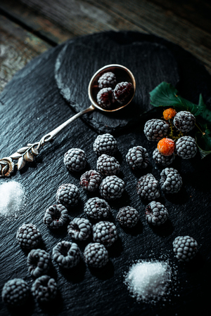 Still life in vintage style. Close up frozen berry of blackberry with spoon and sugar on black stone standの写真素材