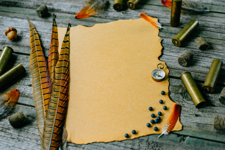 Closeup feather and cartridges on vintage paper for information on old wooden background. Hunting equipment on vintage board. Top viewの写真素材