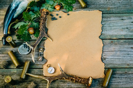 Vintage paper for information on wooden background and deer horn and powder flask beside. Hunting equipment on old board. Top viewの写真素材