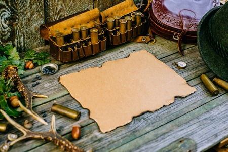 Vintage paper in the center of hunting equipment, oak and horns around of old wood board. side viewの写真素材