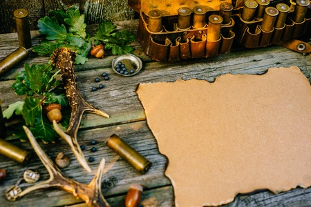 Closeup vintage paper in the center of hunting equipment, oak and horns around of old wood board. side viewの写真素材