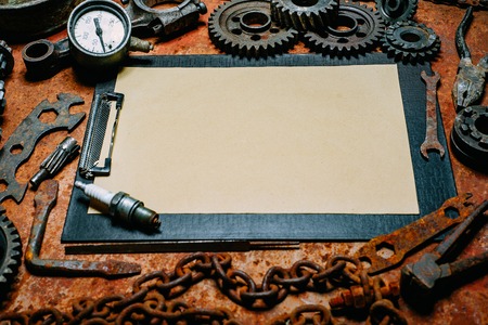 Clipboard with vintage paper in the center of rusty tools, gears on old metal background. Motorcycle tools, equipment and repair. Horizontal backgroundの写真素材