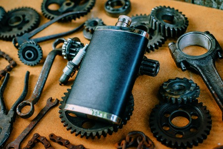 Square black flask in the center of rusty tools, gears on vintage background. Motorcycle equipment...