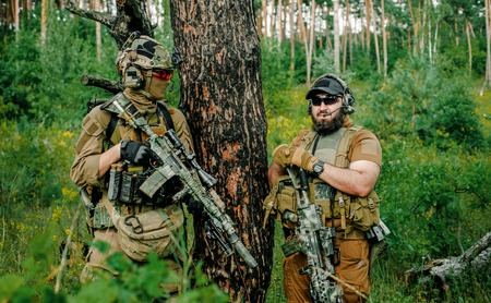 Airsoft men with guns stand back to back. Soldiers stand on hill and on call in the forestの写真素材