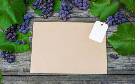 Vine with grapes and leaves on vintage rustic wooden table. Paper tag on old paper template in center top viewの写真素材