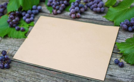 Vine with grapes and leaves on vintage rustic wooden table. Paper tag on leaves and old paper template in center.の写真素材