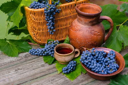Baskets and bowl with grapes beside Jar and cup with wine stand on rustic wood. Wine making background.の写真素材