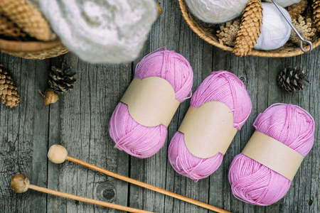 Three pink balls of wool threads with empty labels lying on vintage wood desk with knitting needles...