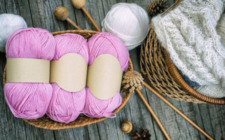 Hand put knitting work on basket and ball on desk. Close up two pink balls of wool threads with...