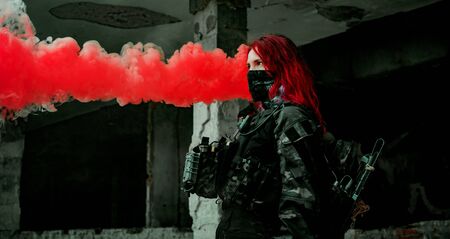 Airsoft red-hair woman in uniform with red smoke in hand. Close up soldier in broken building....