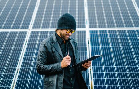 Closeup man stand beside of solar panels with clipboard in hand and make notes.の写真素材