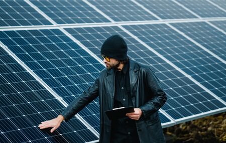 Man with clipboard stand beside solar panels and check surface by hand