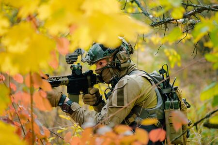 Closeup man in uniform move with machine gun through yellow forest. Airsoft soldier in forest side view.の写真素材