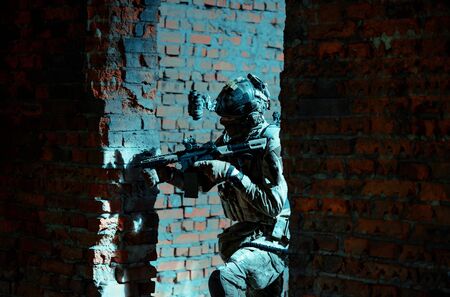 Man in uniform with machine gun and night-vision device move between two broken walls. Airsoft soldier in night building.の写真素材